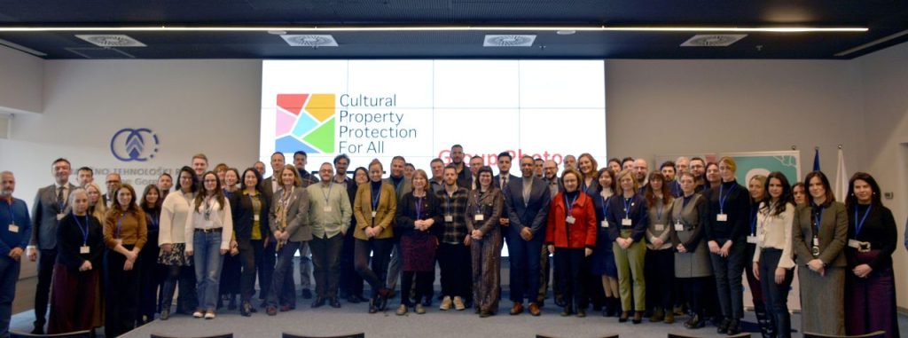 A large group of conference goes standing in front of a screen that says Cultural Property protection for all.
